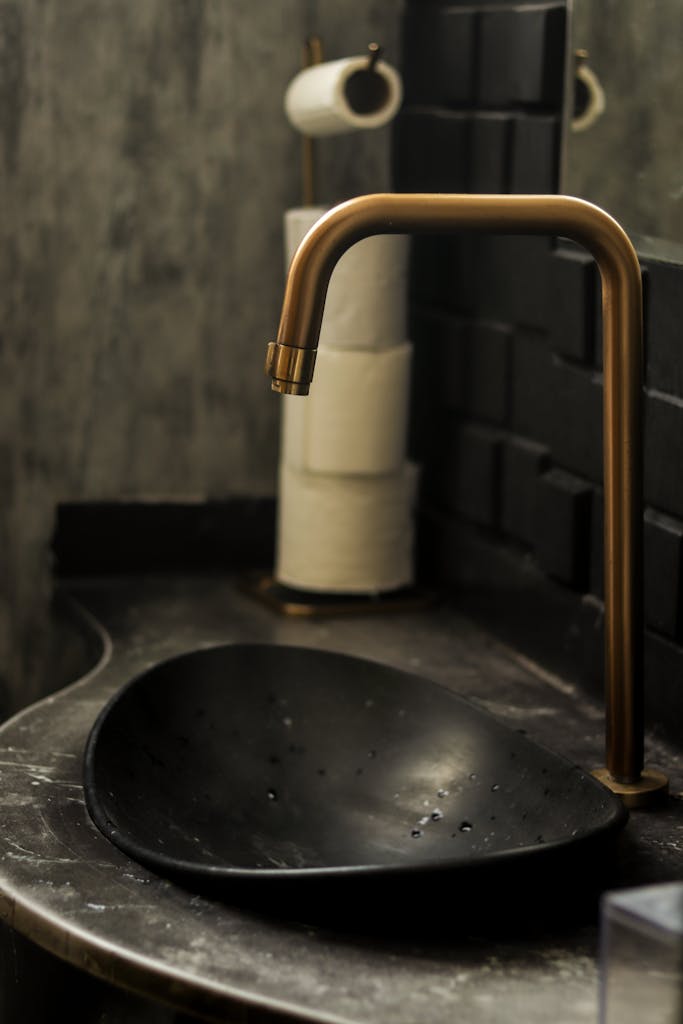 A modern bathroom sink with a sleek black basin and brass faucet, complemented by a stylish interior design.